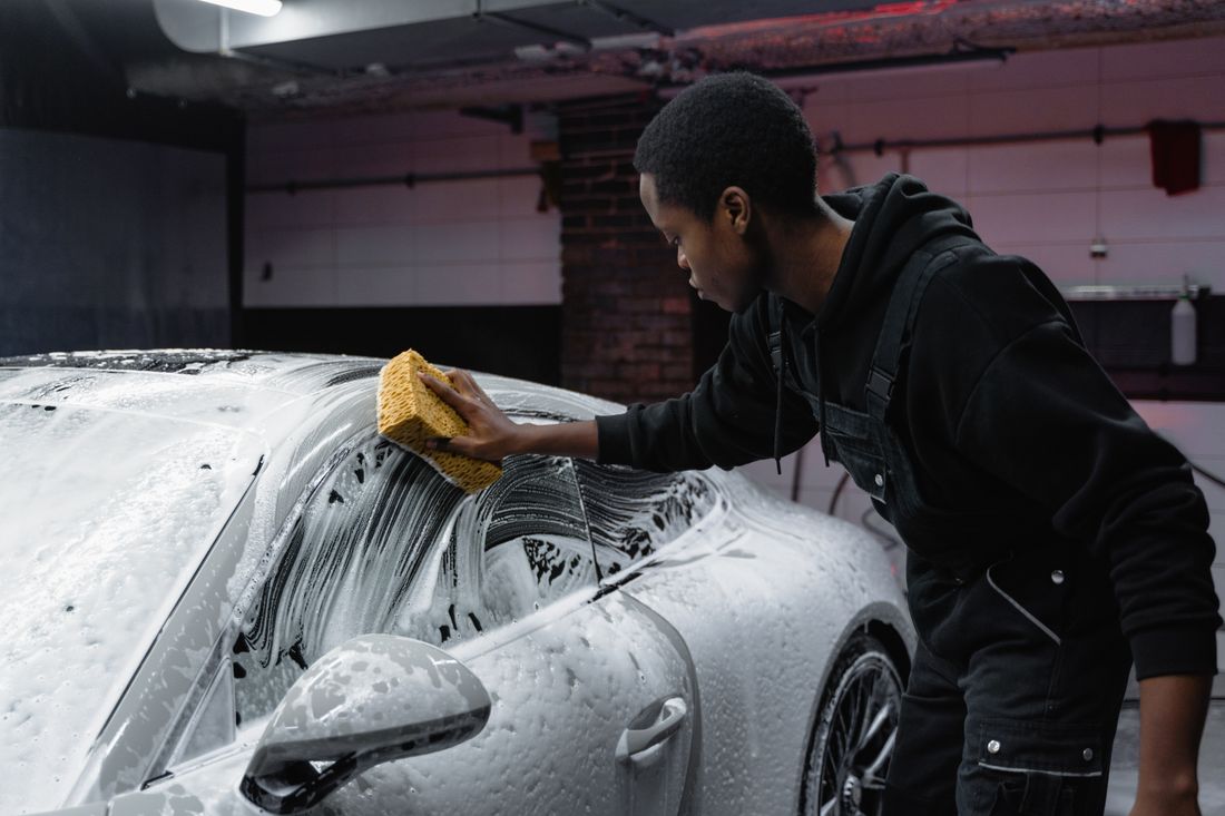 Detailer hand washing a foam-covered sports car