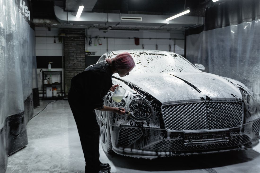 Detailer hand washing a foam-covered luxury car