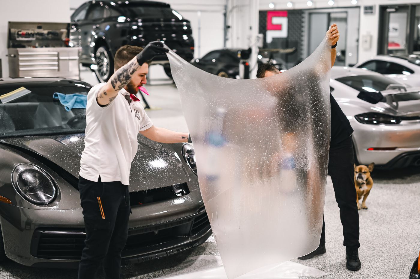 Two installers laying paint protection film on a Porsche
